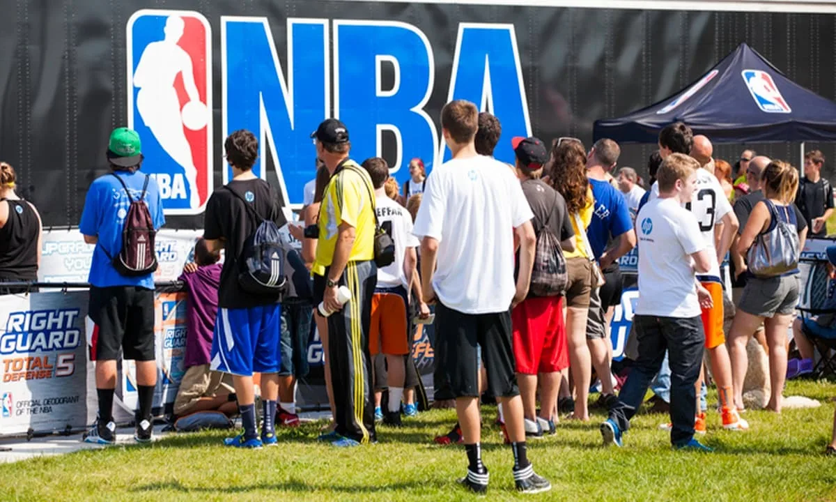 NBA Costs A group of people standing near a large blue NBA logo.