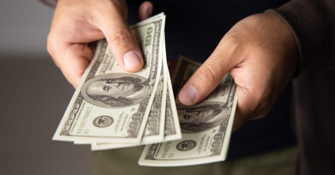 Person holding several $100 dollar bills