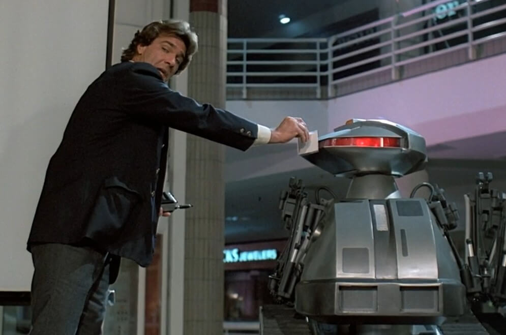 A man in a suit holds out a badge for a robot to scan.