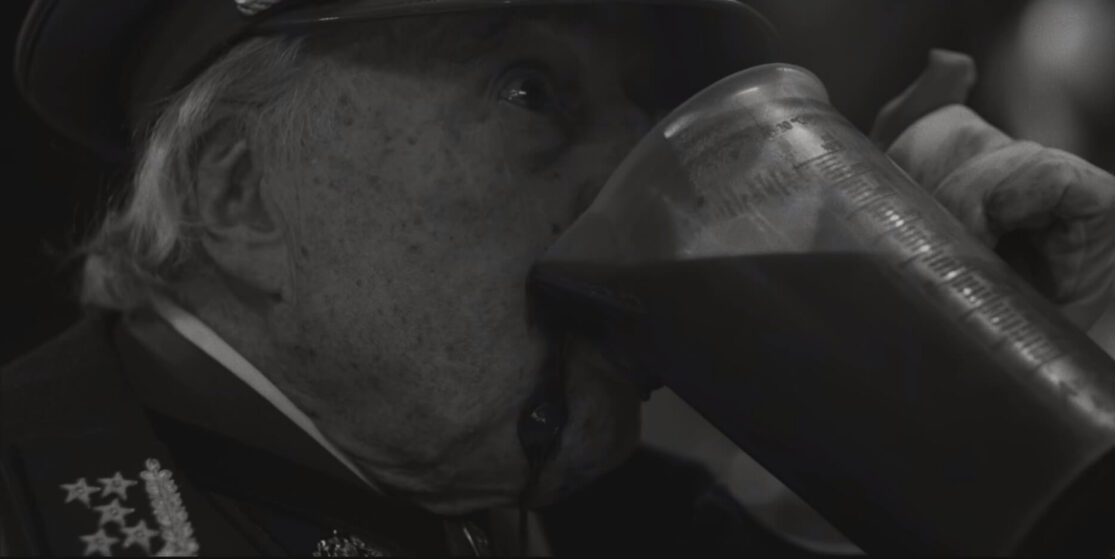 A close up of an old man in a military uniform sloppily drinking a pitcher of blood.