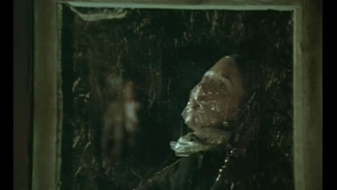 A young woman, seen through a windowpane, appears to have been smothered by a plastic bag.