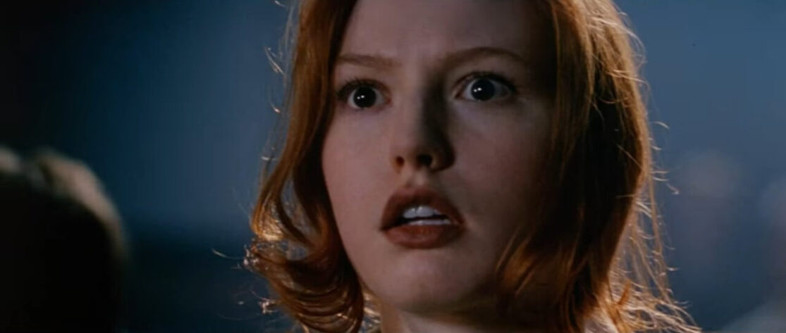 A close-up of a fearful young redheaded woman's face at night.