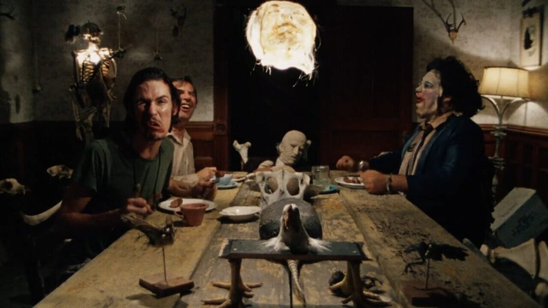 An all-male family sits at the dinner table laughing and making faces. Over the table hangs a macabre lamp made from someone's face.