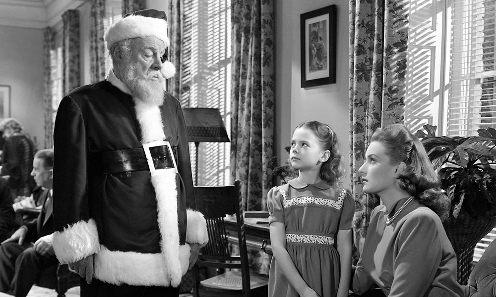 Santa looks down at a little girl and her mother; the picture is in black and white.