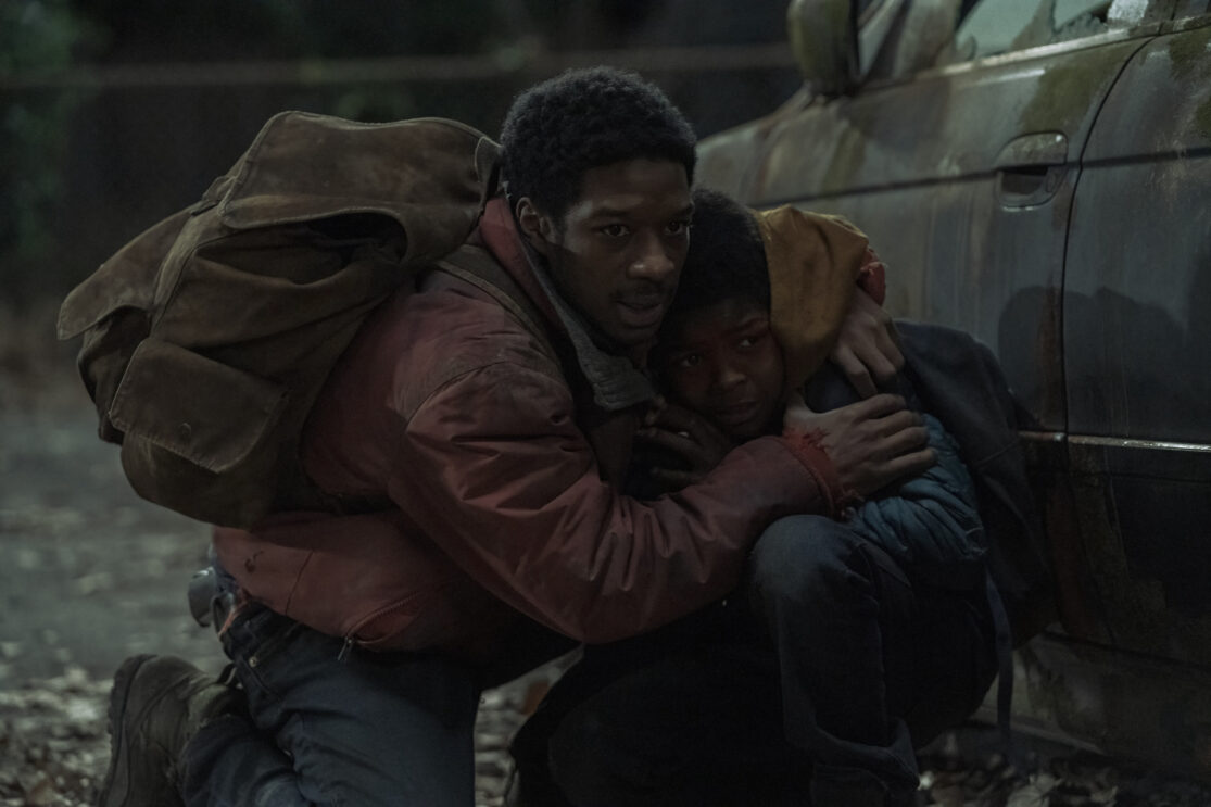 Lamar Johnson and Keivonn Woodard crowding behind a car in HBO's The Last of Us