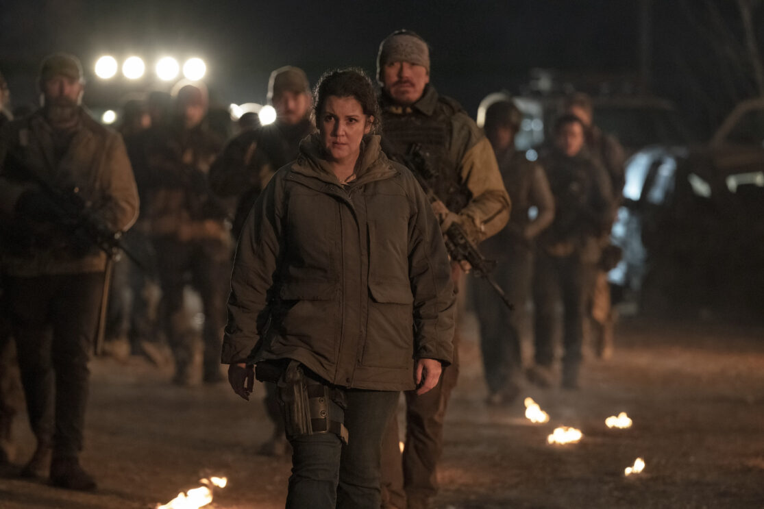 Melanie Lynskey standing in front of a crowd of soldiers in HBO's The Last of Us.