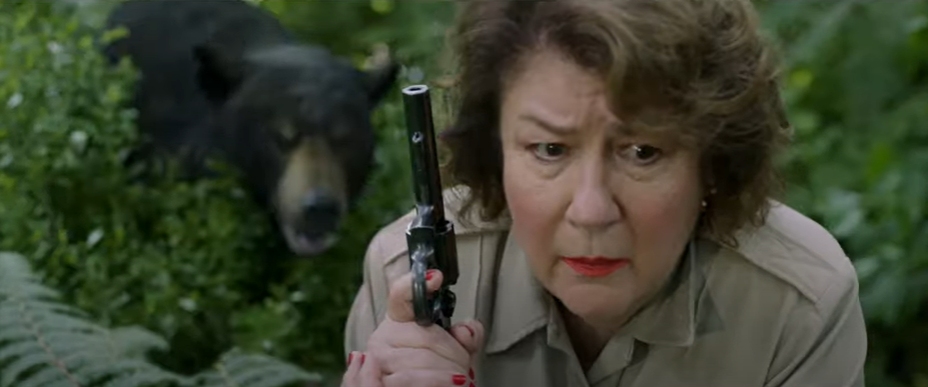 Margo Martindale holding a gun, hunting the Cocaine Bear—but it's right behind her.