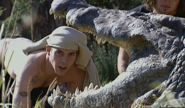 Young man with shirt on his head looking in open mouth of crocodile