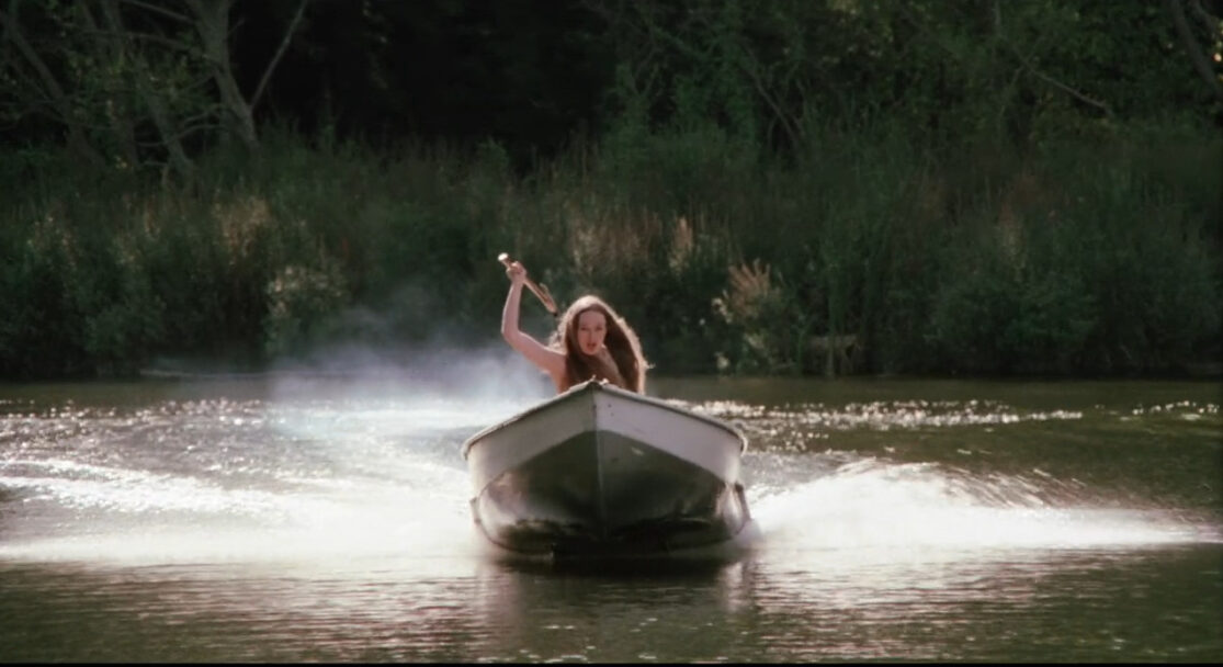 A woman holding an axe speeds toward an unseen victim in a motorboat.