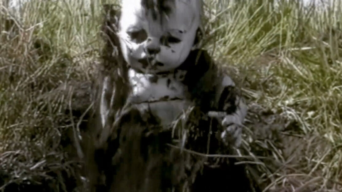 A pale, dirty baby doll digs its way out of a grave.