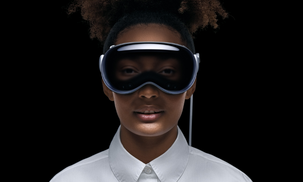 A forward-facing portrait of someone wearing the Apple Vision Pro, which looks like a VR headset, except that it displays a rendering of the person's covered eyes on the outside.