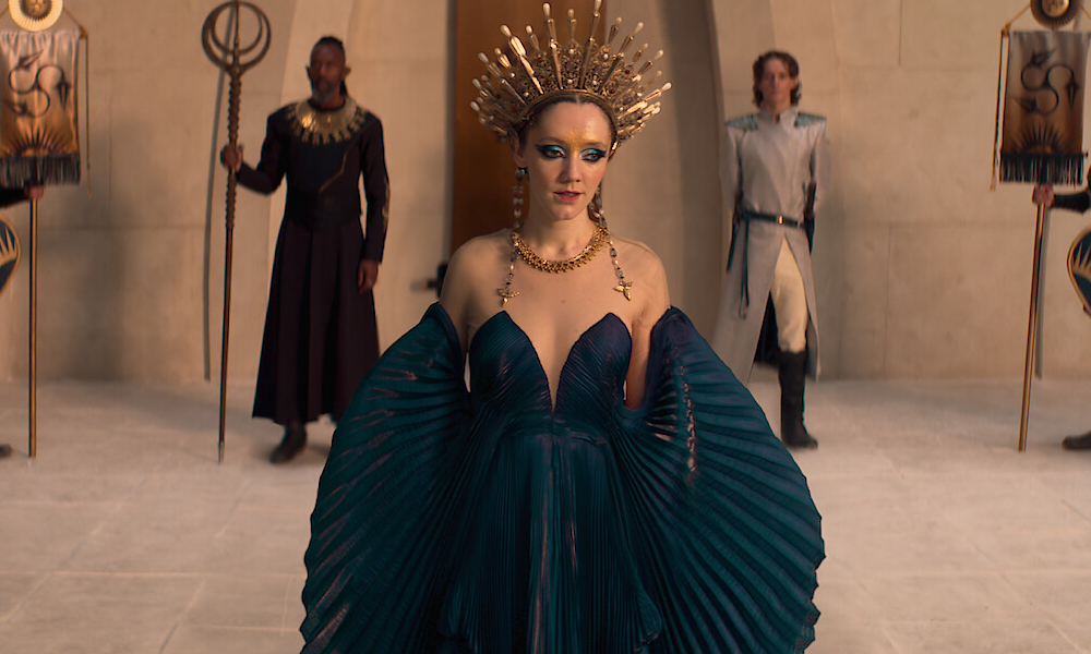 Merwyn, an elf woman wearing a large golden crown and a navy blue gown.