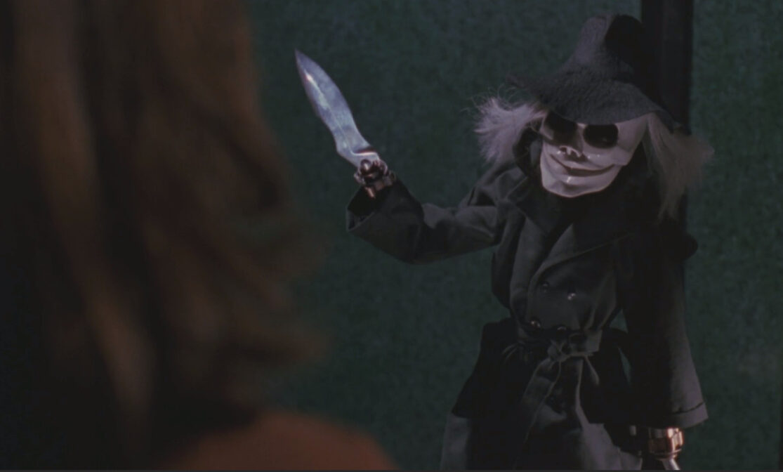 A cloaked puppet threatens a woman with a knife in Puppet Master.