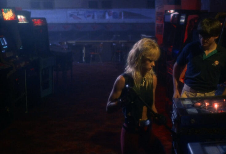 In a 1980s-era arcade, a male nerd and a female punk rocker try to break into a pinball machine.