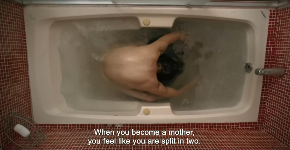 A pregnant woman doubled over in a bathtub with her back to the camera, which is above her. Subtitles read: "When you become a mother, you feel like you are split in two."