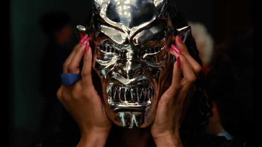 A woman's tries on a shiny demonic mask.