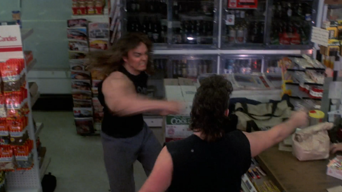 A long-haired man in a muscle shirt punches an armed robber in a convenience store.