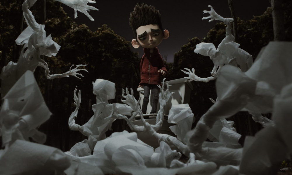 Norman, a stop-motion animated boy with sticky-uppy hair, looking sadly at some ghouls.