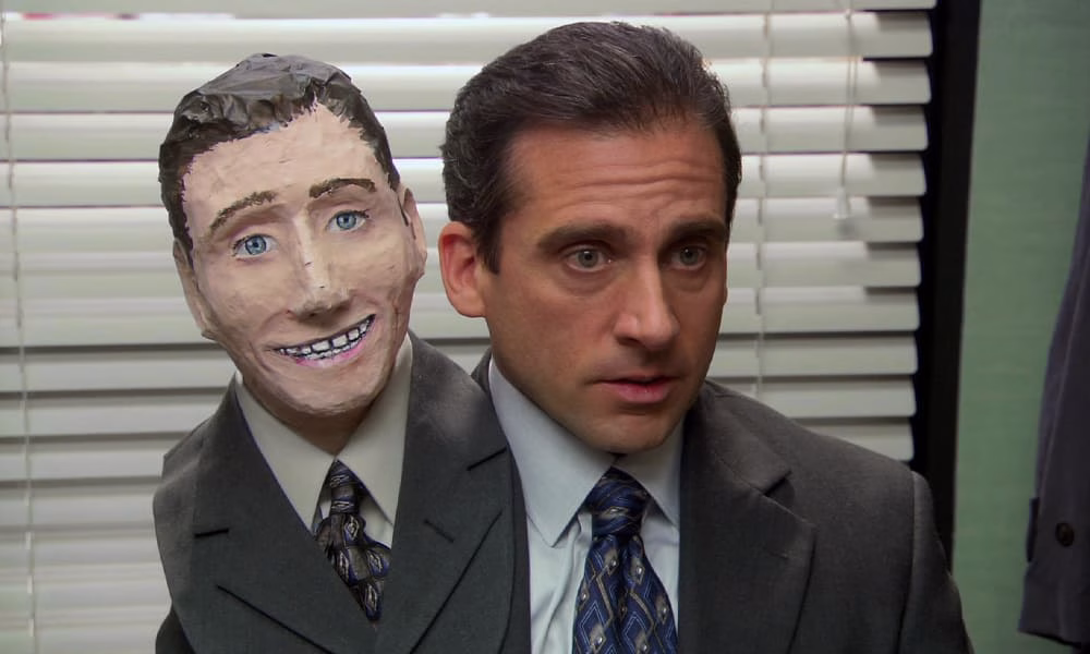 Best Halloween TV Episodes - The Office Steve Carell as Michael Scott wearing a second head made of paper mache in one of the best Halloween TV episodes from The Office.