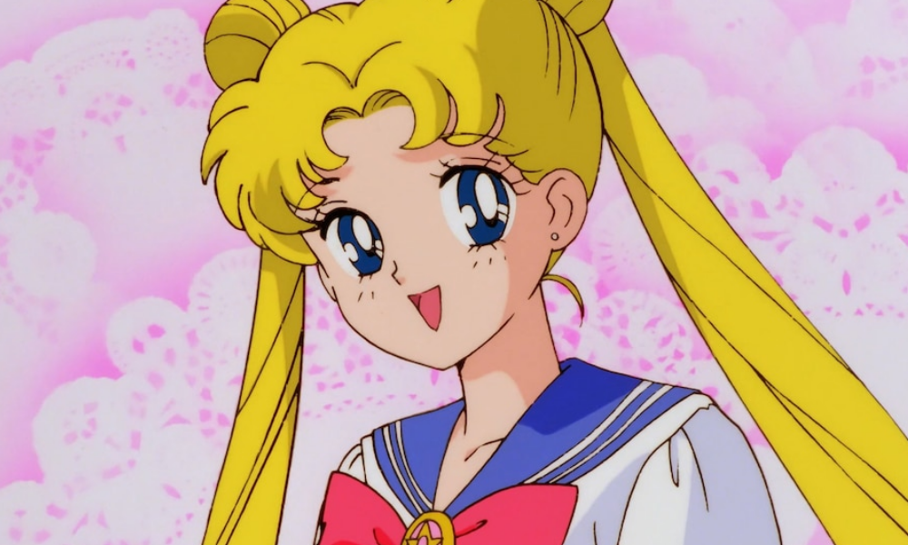 Usagi, an anime girl with long blonde hair in two buns, wearing her sailor-style school uniform in front of a pale pink background.