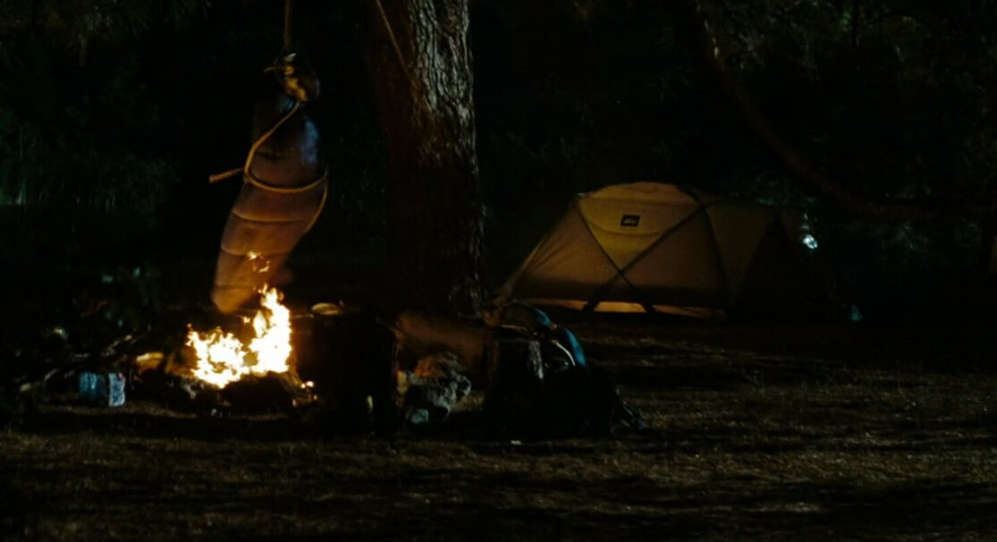 A camping scene where a hanging sleeping bag swings over the campfire.