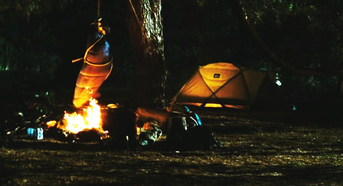 A sleeping bag swings over a campfire at night.