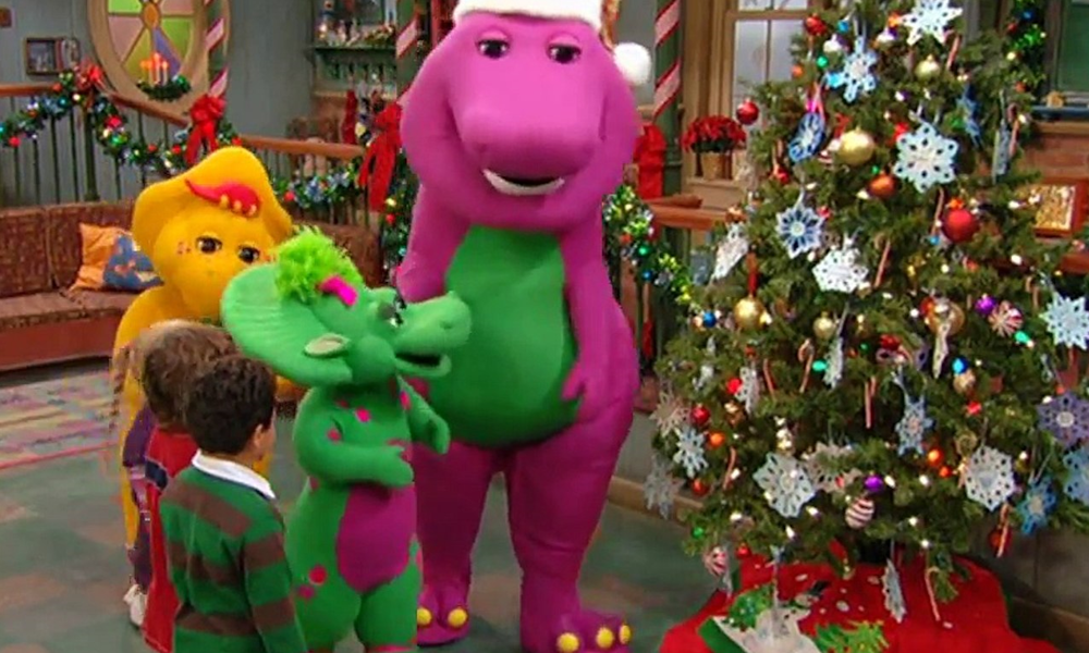 Barney, a purple dinosaur, next to a Christmas tree.