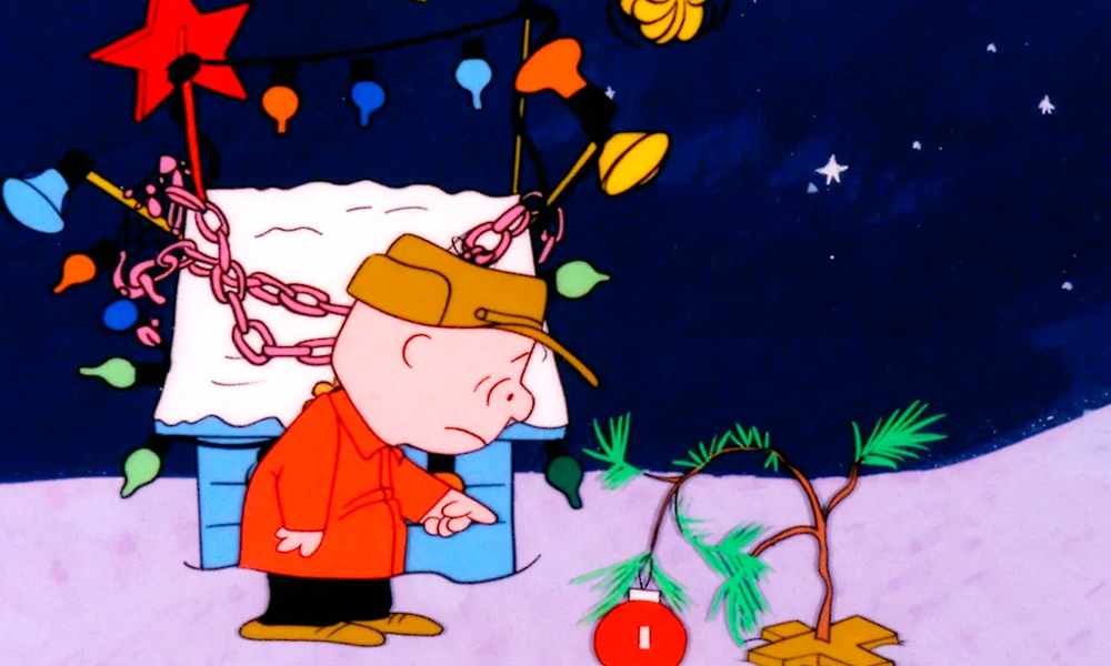 Charlie Brown looks despairingly at a tiny tree bowing under the weight of an ornament.