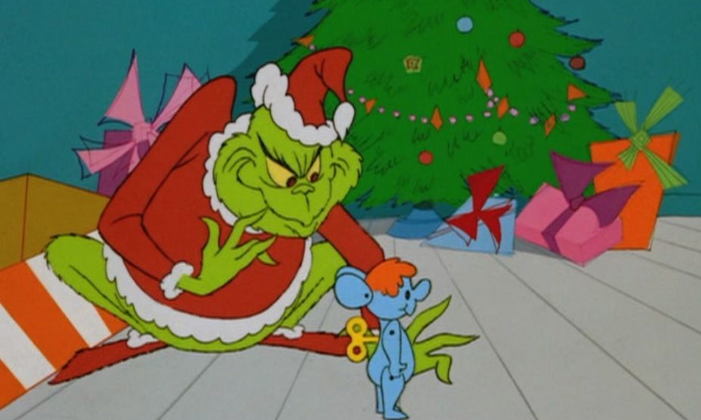 The Grinch, dressed as Santa, sets up a blue wind-up toy.