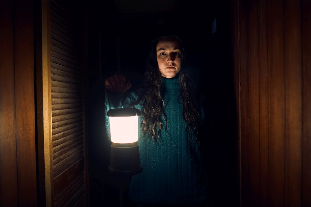 A young woman walks through a dark hallway with a lantern