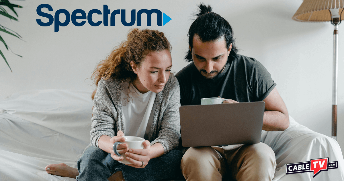 Couple sitting on edge of bed studying laptop screen while sipping coffee