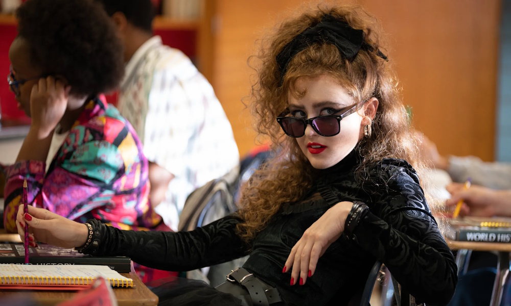 Lisa Frankenstein, a teenager with curly red-brown hair styled in 1980s fashion wearing black sunglasses and a black lacy mourning outfit.