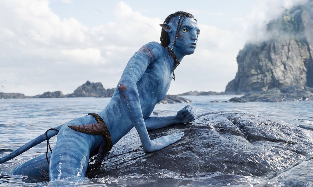 A blue-skinned boy rests on the back of an alien creature in the ocean.