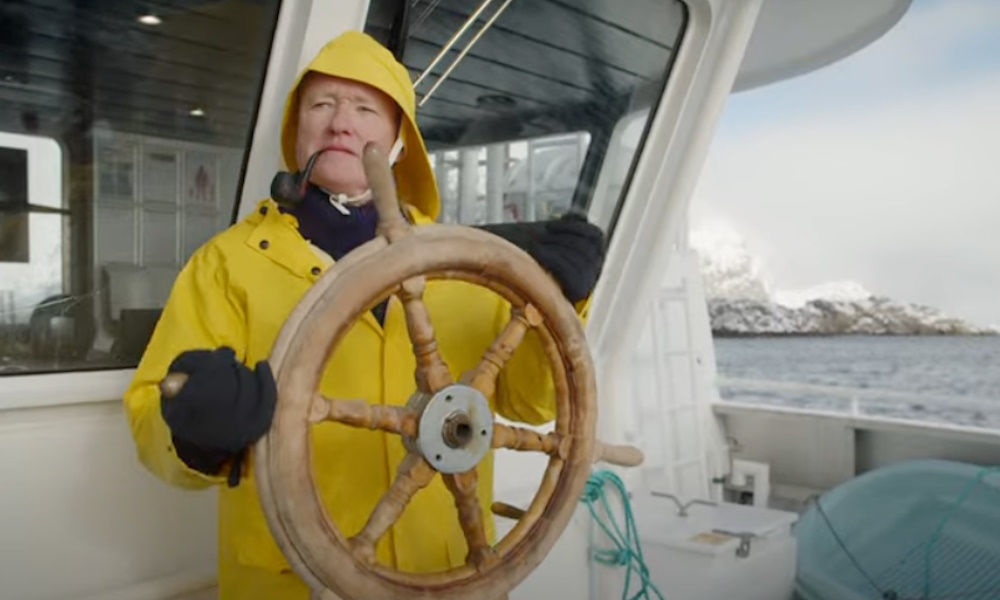 Conan O'Brien wearing a yellow raincoat on a boat.