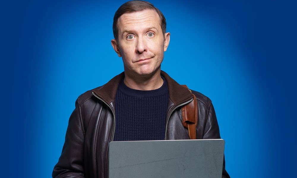 A man looking at the camera with an awkward smile on a blue background. The man is Tim Downie.