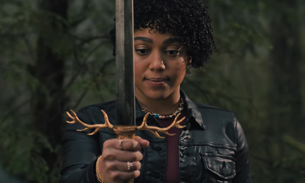 A woman with curly hair holding a sword with deer antlers at the pommel.