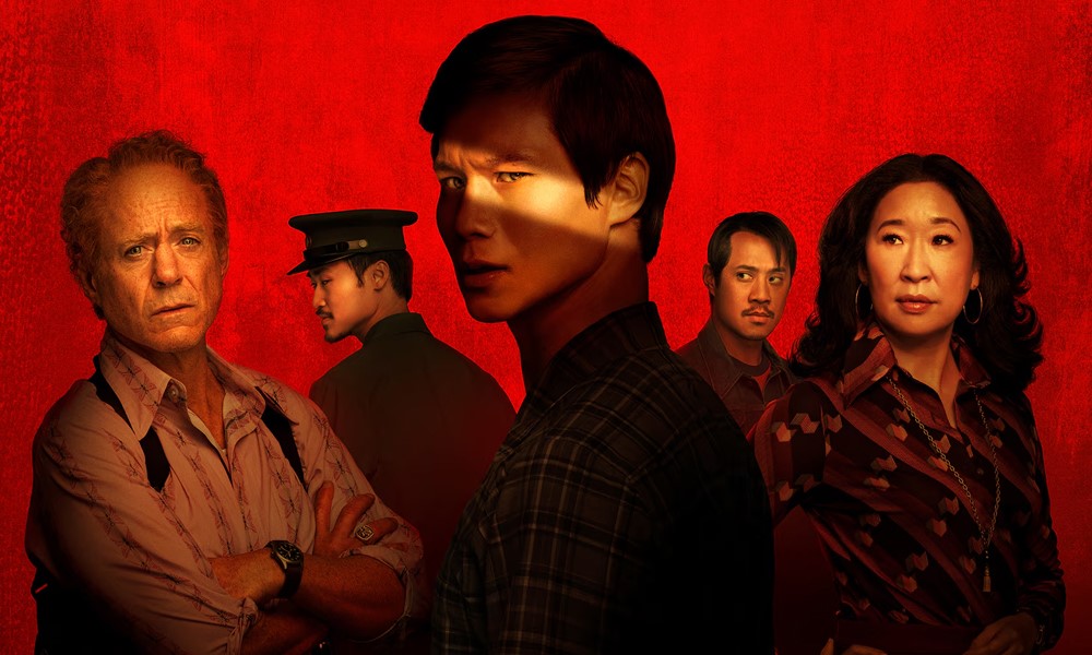 Several people stand in front of a red background; the man in front has a dramatic beam of light across his face.