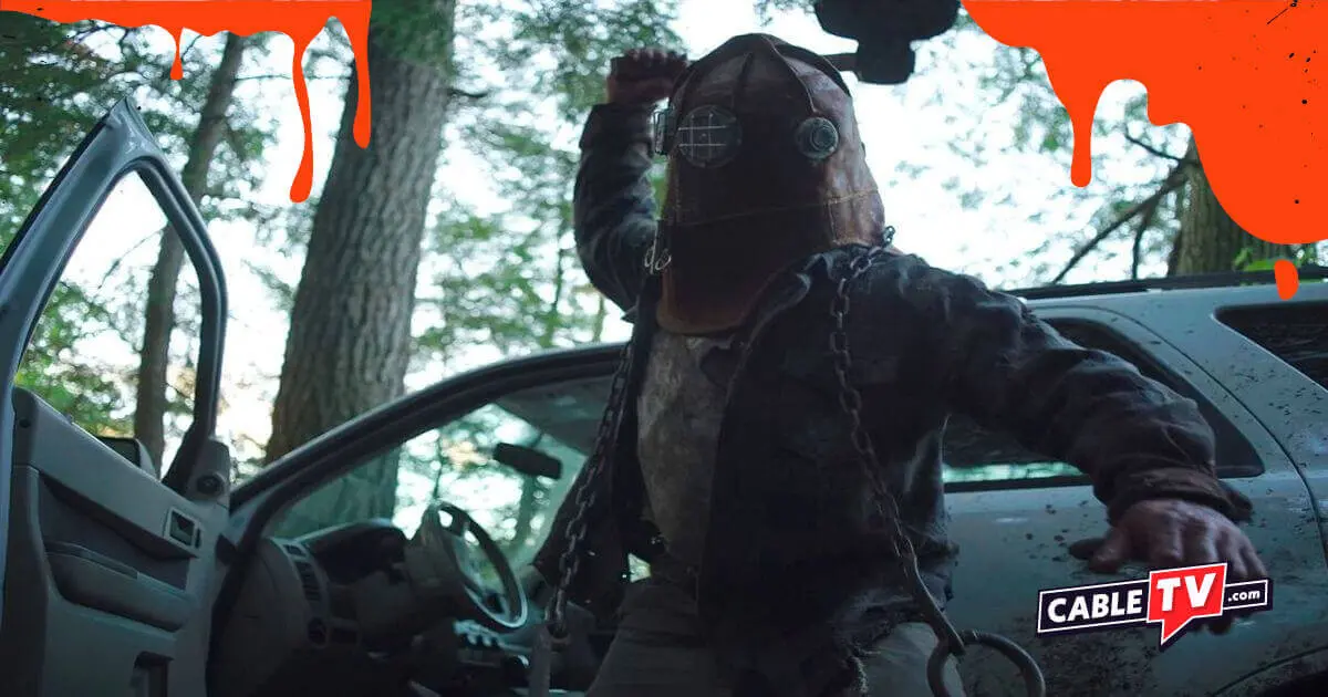 A man in an old firefighter's mask raises a weapon in a scene from In A Violent Nature.
