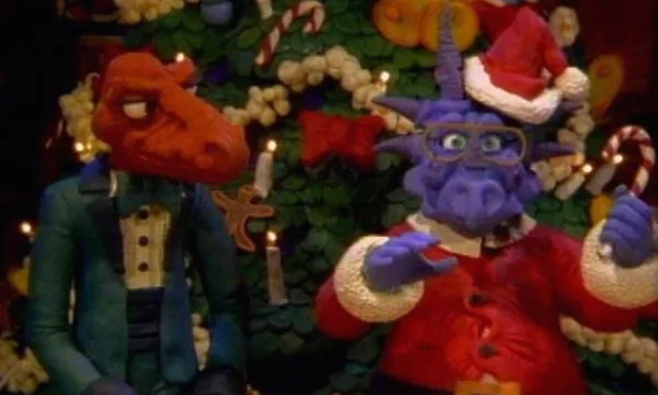 Claymation dinosaurs Rex and Herb, dressed in a tuxedo and Santa suit respectively, stand in front of a Christmas tree in the 1987 special.