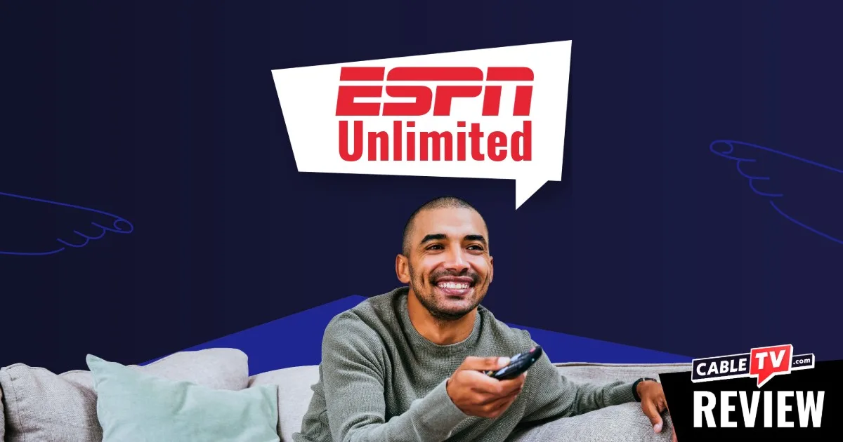 Man sitting on a couch and smiling while pointing a remote control towards the camera