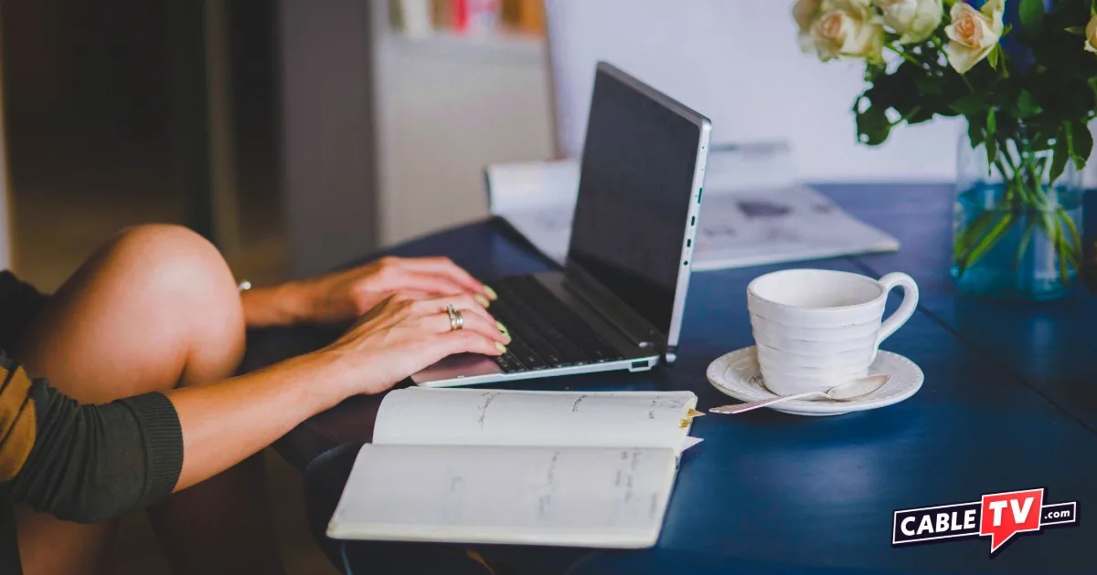 Woman sitting at a table with a laptop and open notebook