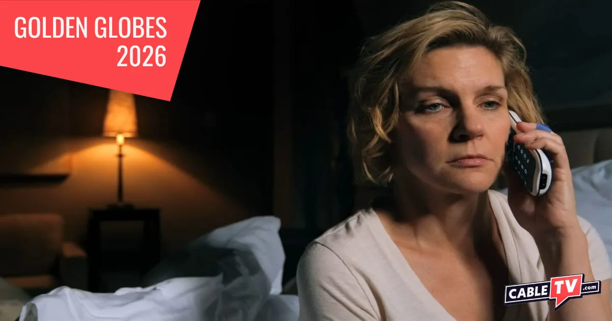 A depressed woman sits on her bed talking on the telephone.