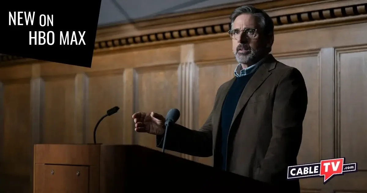 A man addresses a class from behind a podium in a college lecture hall.
