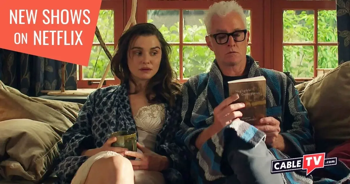 A man and a woman sit on their couch drinking coffee and looking at a book.
