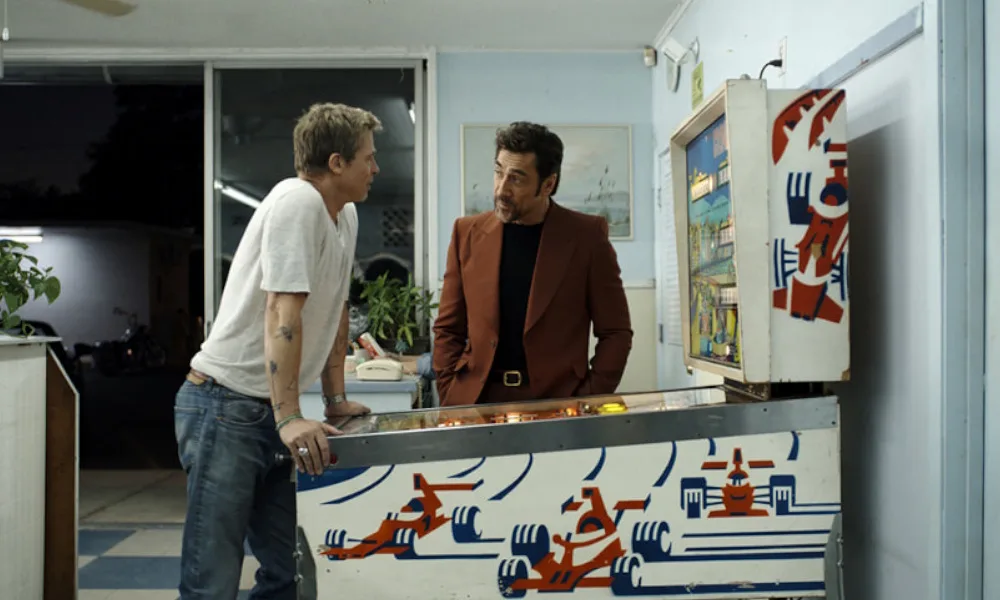 F1_1000x600 Two men stand around a pinball machine.