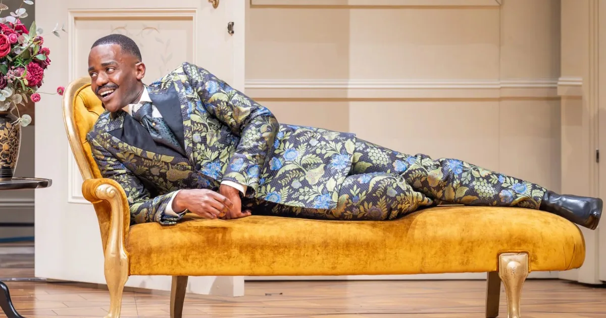 Ncuti Gatwa reclining on a sofa while wearing a vividly patterned suit.