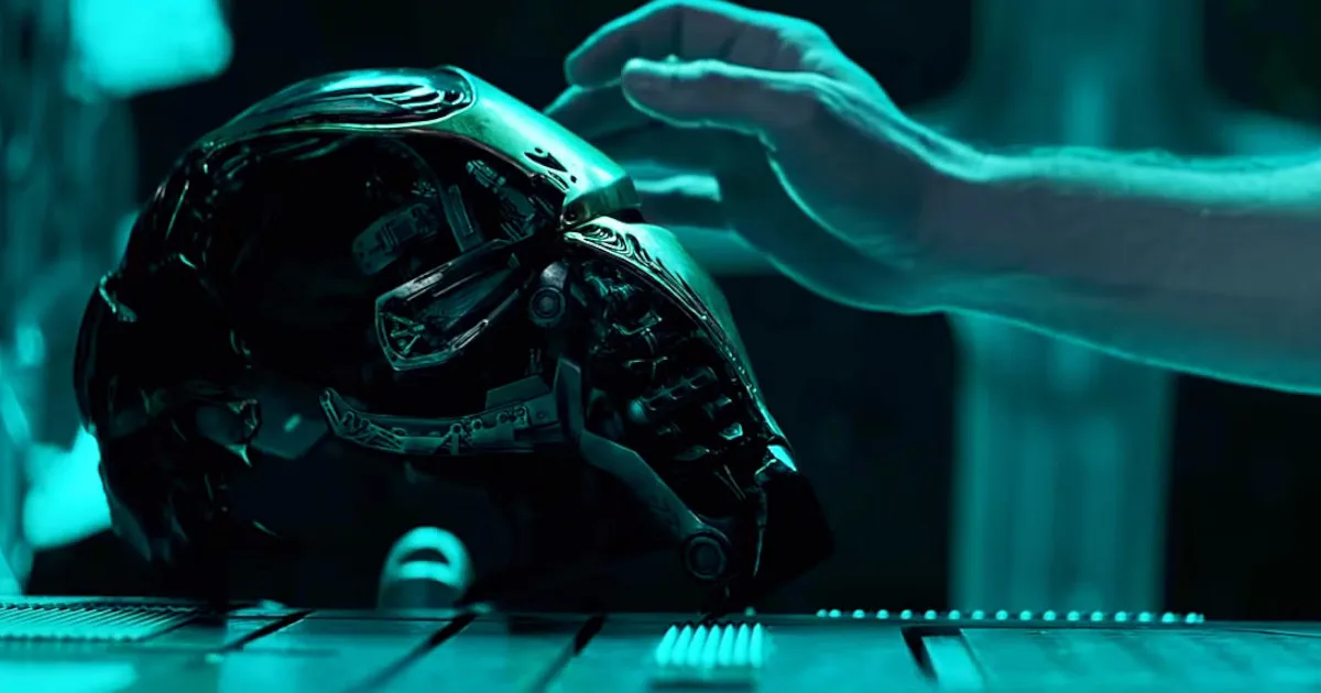A hand reaches towards Tony Stark's busted Iron Man helmet.