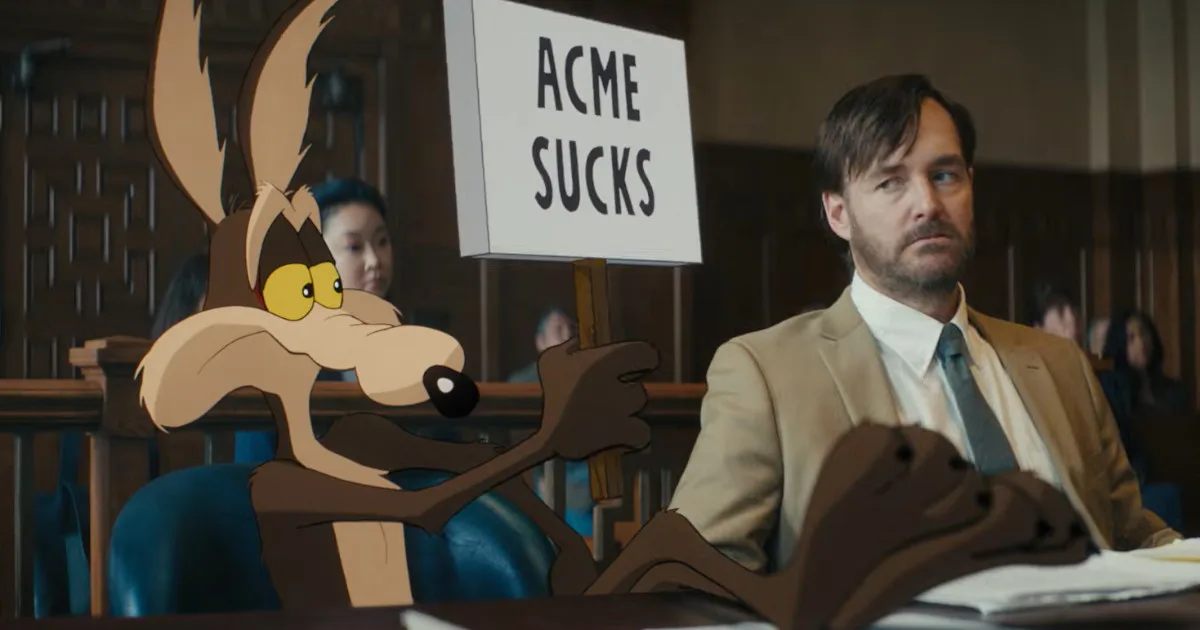 Wile E. Coyote, a cartoon, holds up a sign that says "ACME Sucks." His lawyer, real live-action man Will Forte, looks upset.