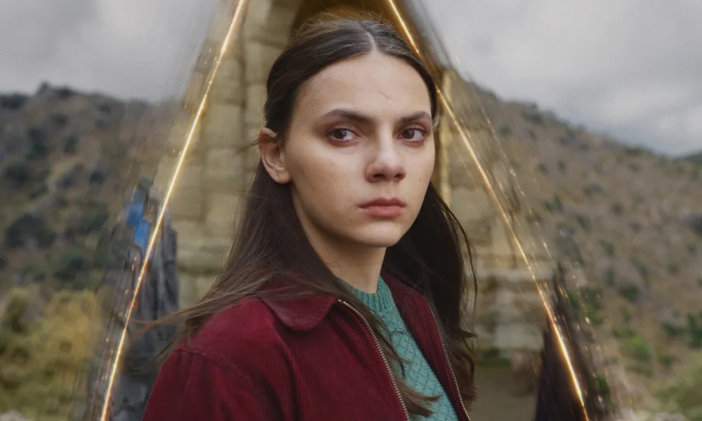 HisDarkMaterials1000x600 A teenage girl stares sadly into the distance with magical streaks of light behind her.