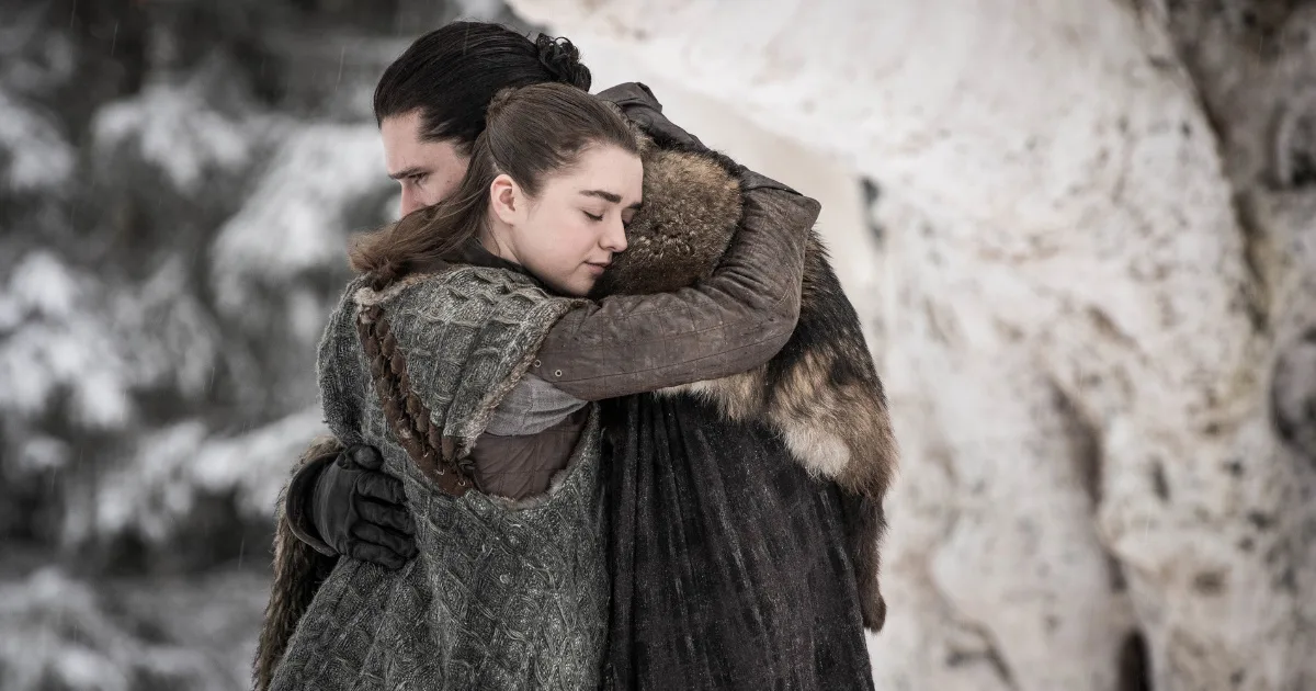 A man (Jon Snow) and a young woman (Arya Stark) hug in the wintery woods.